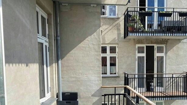 A balcony with a wooden floor, metal railing, and a table with chairs. - Classic apartment with a balcony in Amagerbro (København)