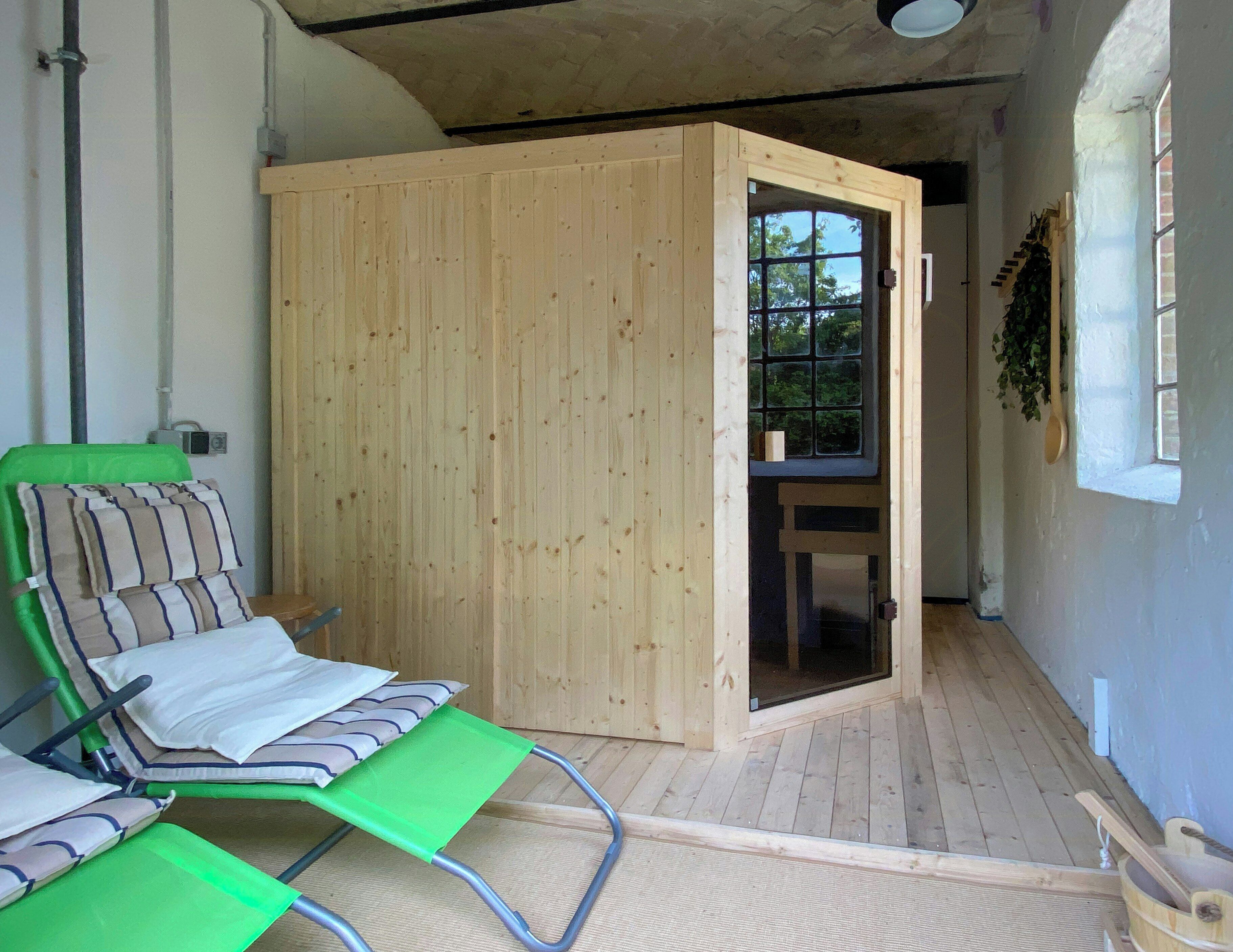 A room with a wooden door, a green chair, a wooden bench, and a window with a view of trees.