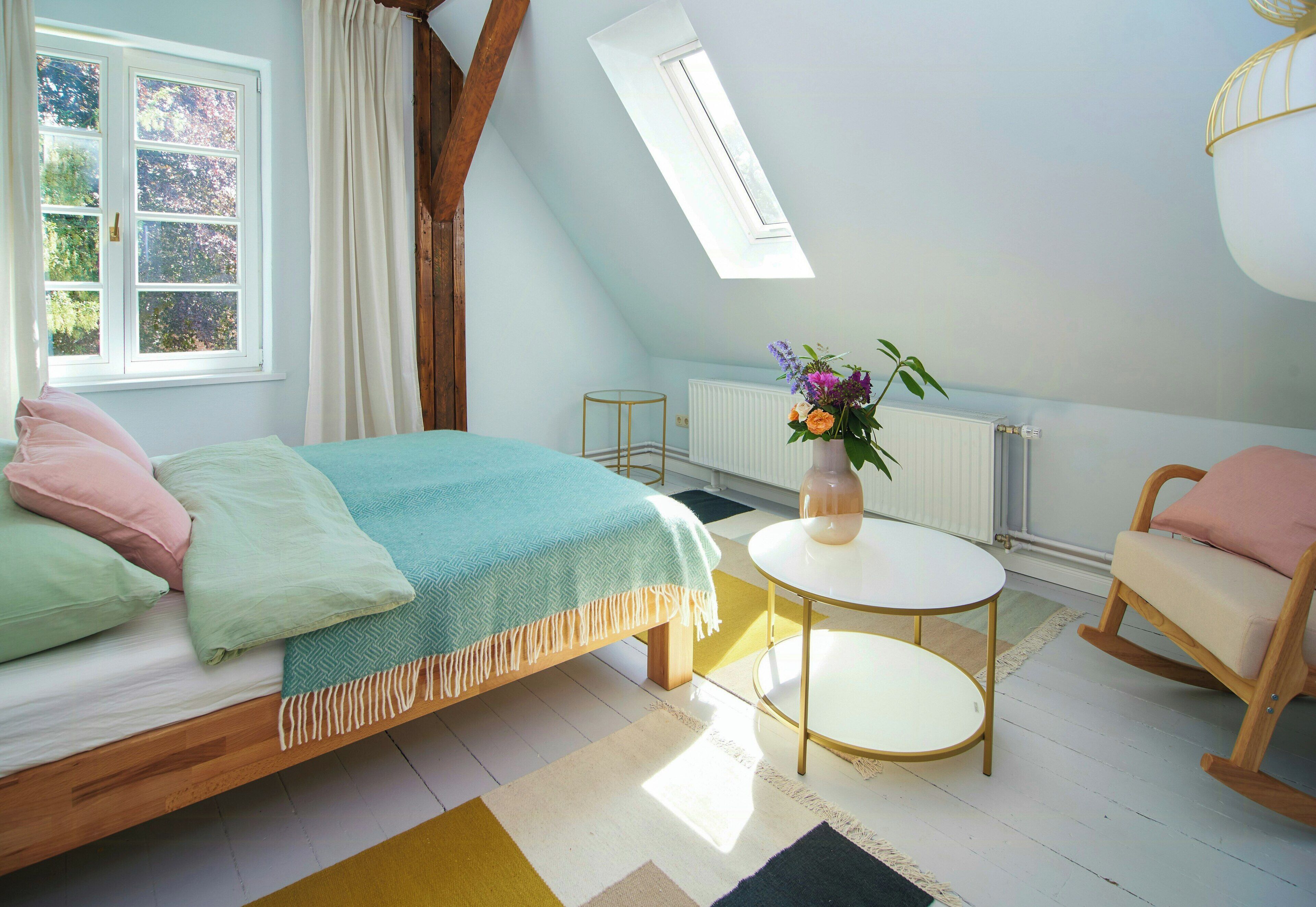 Ein Schlafzimmer mit einem Bett, einem runden Tisch, einem Schaukelstuhl, einem Fenster und einem Dachfenster.
