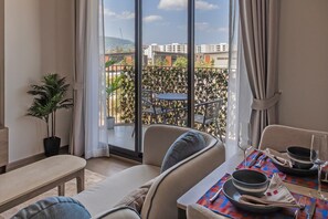 A hotel room with a balcony, a dining table set with plates and glasses, a bench, and a potted plant. - Bright 2-bedroom apartment in center of Bangtao (Tambon Choeng Thale)