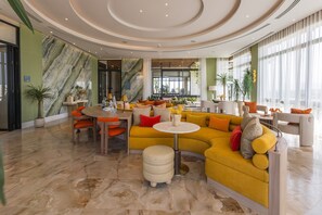 Un moderno vestíbulo de hotel con un sofá amarillo, mesas redondas y una pared de mármol.