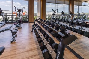 Un gimnasio con equipamiento de ejercicio, ventanas amplias y vistas a la ciudad.