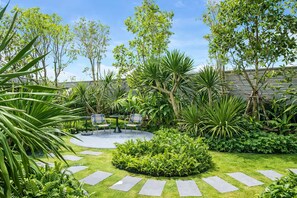 A garden with a circular seating area, surrounded by various plants and trees. - Bright 2BR Apartment in Central Bang Tao (Choeng Thale)