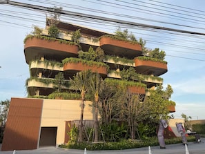 Un immeuble à plusieurs étages doté de balcons couverts de verdure, d’une entrée en béton et d’un espace paysager agrémenté d’arbres.