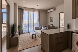 A modern apartment with a living area, kitchenette, and a balcony with a city view. - Bright 2-bedroom apartment in center of Bangtao (Tambon Choeng Thale)