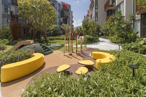 Un espace de jeux pour enfants avec des structures en matériaux souples, des sièges et un jardin agrémenté de différentes plantes.