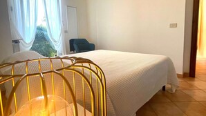 Quarto de hotel com cama, cadeira, janela com cortinas e vista para o verde lá fora.