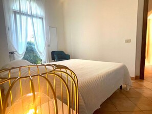Ein Hotelzimmer mit Bett, Stuhl, Fenster mit Vorhängen und Blick auf Grünfläche.