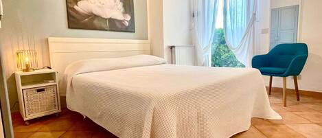 A bedroom with a bed, a nightstand, a chair, and a window with curtains.