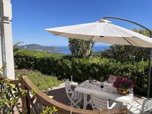 Une terrasse extérieure avec une table et des chaises, un parasol et une vue sur la mer et les collines.