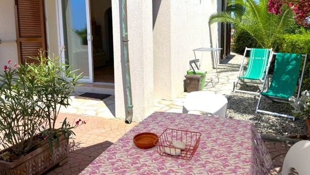 Uma área de pátio com mesa, cadeiras, um pequeno jardim e entrada de um edifício.