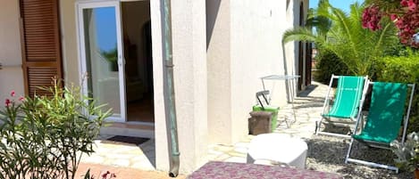A patio area with a table, chairs, a small garden, and a building entrance.