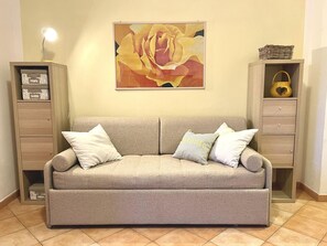 Ein sofasofa in neutralen Farbtönen mit drei Kissen, flankiert von Holzschränken mit Schubladen und Regalen, vor einer schlichten Wand mit einem gerahmten abstrakten Gemälde.