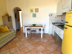 A compact living space with a dining area, kitchenette, and a sofa with patterned cushions. - Malea - MALEA by ColombiElbaVacanze (Capoliveri)