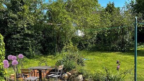 Un patio giardino con tavolo e sedie, immerso nel verde e fiorito.