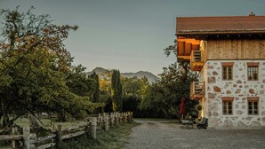 A stone building with a wooden balcony, a gravel path, and a wooden fence. - Living among orchards by Lake Chiemsee (Übersee)