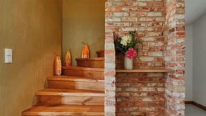 A wooden staircase with a brick wall on one side, a small shelf with flowers, and a striped rug on the floor. - Living among orchards by Lake Chiemsee (Übersee)