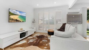 Una sala de estar moderna con un sofá blanco, un televisor de pantalla plana grande, un tapete de cuero de vaca y vistas al océano a través de una ventana.