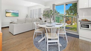 Una sala de estar moderna con un sofá blanco, una mesa de comedor con sillas blancas y un ventanal con vistas al exterior.