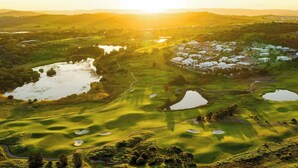 Un campo de golf con búnkeres, obstáculos acuáticos y una zona residencial al fondo.