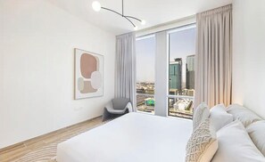 Ein modernes Hotelzimmer mit einem großen Bett, einem Sessel, Blick auf die Stadt und einem gerahmten Kunstwerk an der Wand.