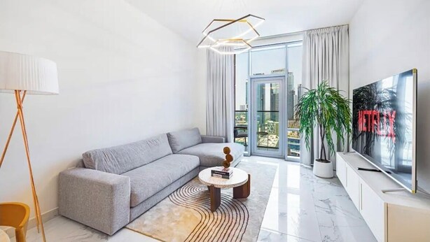 Ett modernt vardagsrum med en grå soffa, ett runt soffbord, en golvlampa, en tv och ett stort fönster med gardiner.