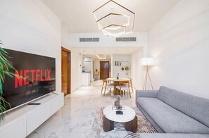 Ein modernes Wohnzimmer mit Flachbildfernseher, einem grauen Sofa, einem runden Couchtisch und einem Essbereich mit Holztisch und Stühlen.