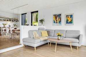 A modern living room with a grey sectional sofa, a round coffee table, and two abstract paintings on the wall. - Summerhouse close to nature by The Limfjord (Nykøbing Mors)