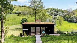A rustic cabin with a wooden deck leading to the entrance, surrounded by lush greenery and hills. - Summerhouse close to nature by The Limfjord (Nykøbing Mors)