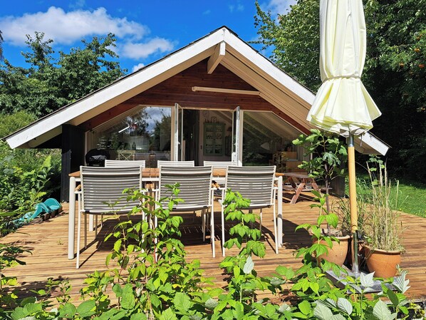 Eine Holzterrasse mit Gartenmöbeln, einem überdachten Sitzbereich und Topfpflanzen.