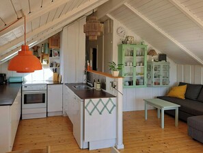 Une cuisine compacte dotée d’un îlot central, d’un coin repas avec un banc et d’un espace nuit en mezzanine avec un canapé.