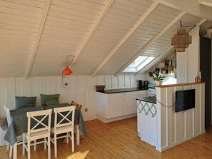 Ein gemütliches Dachzimmer mit Esstisch, Stühlen, einer Küchenzeile mit Herd und einem Oberlicht.