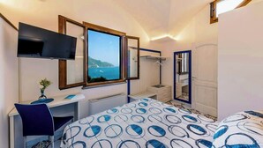 A bedroom with a bed, a desk, a chair, a TV, a window with a view, and a mirror. - Baroque house with lemon groves in Amalfi (Amalfi)
