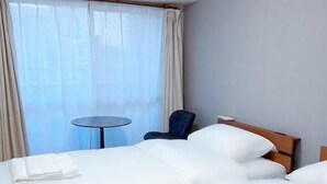 Ein Hotelzimmer mit zwei Betten, einem runden Tisch, einem Stuhl und einem Fenster mit Vorhängen.