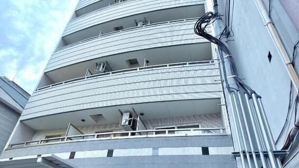 Ein mehrstöckiges Gebäude mit moderner Architektur, mit Balkonen auf jeder Etage, einem überdachten Eingang und einem Bereich für Fahrradstellplätze.
