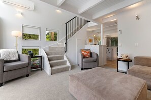 Ein modernes Wohnzimmer mit Treppe, grauen Sofas, einem Couchtisch und einer Küchenzeile im Hintergrund.