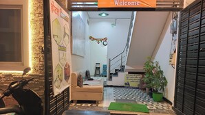 A reception area with a 'Welcome' sign, a sofa, a potted plant, a scooter, and a staircase leading to an upper floor.