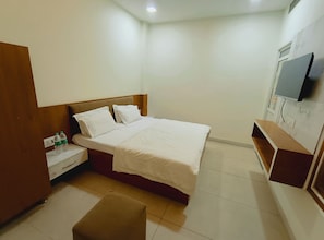 Quarto de hotel com cama, mesa de cabeceira, televisão fixada na parede e um banco de madeira.