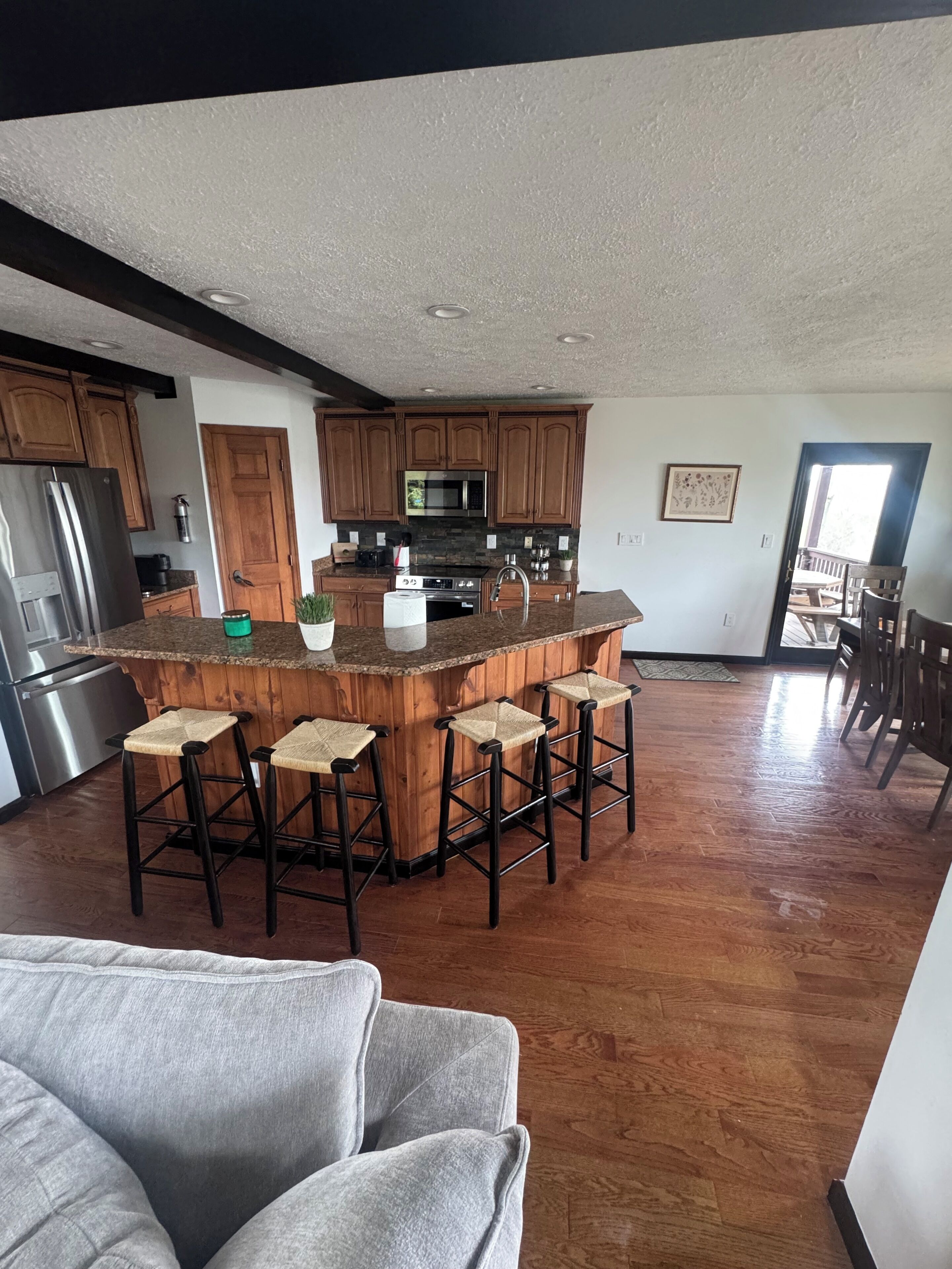 A modern kitchen with a central island, wooden cabinets, stainless steel appliances, and a bar stool seating area.