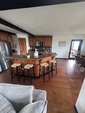 A modern kitchen with a central island, wooden cabinets, stainless steel appliances, and a bar stool seating area.
