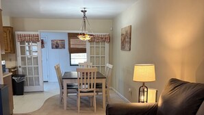 A living room with a brown leather sofa, a dining table with chairs, a chandelier, and a lamp.