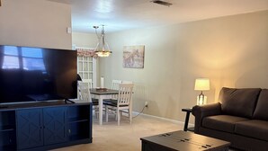 A living room with a TV, a dining table, chairs, a sofa, a coffee table, and a lamp.