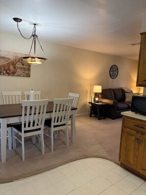 A dining area with a wooden table and white chairs, a chandelier, a painting of a horse, a clock, and a leather sofa. - Stay at our spacious 4-bedroom 2 bathroom house in Childress with AC. (Childress)
