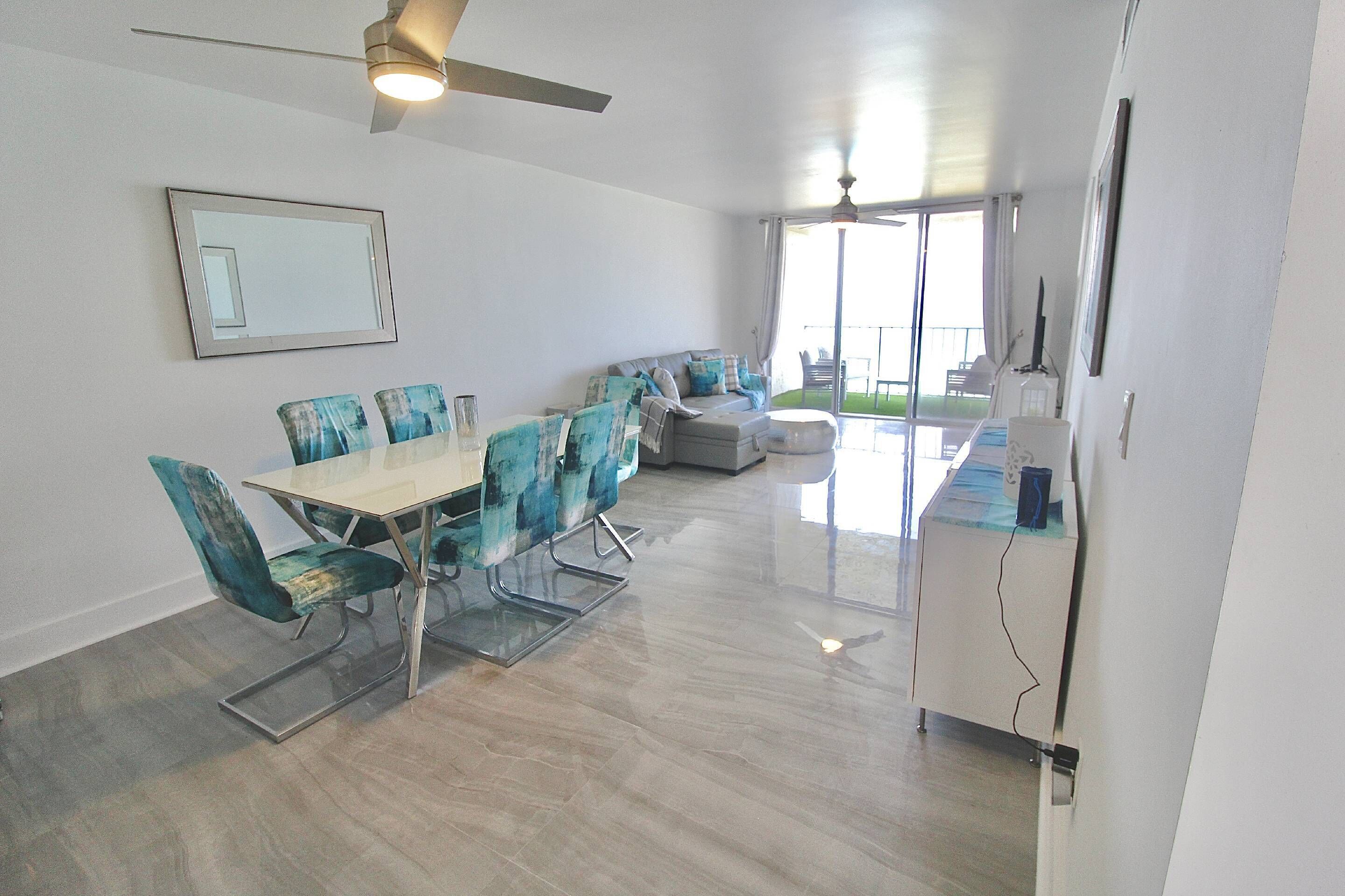 A modern dining area with a glass table and chairs, a sofa, and a ceiling fan.
