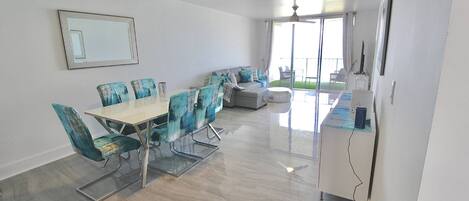 A modern dining area with a glass table and chairs, a sofa, and a ceiling fan.