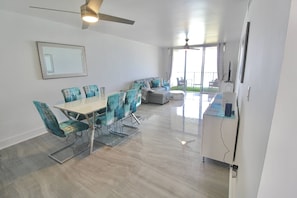 Un comedor moderno con una mesa y sillas de vidrio, un sofá y un ventilador de techo.