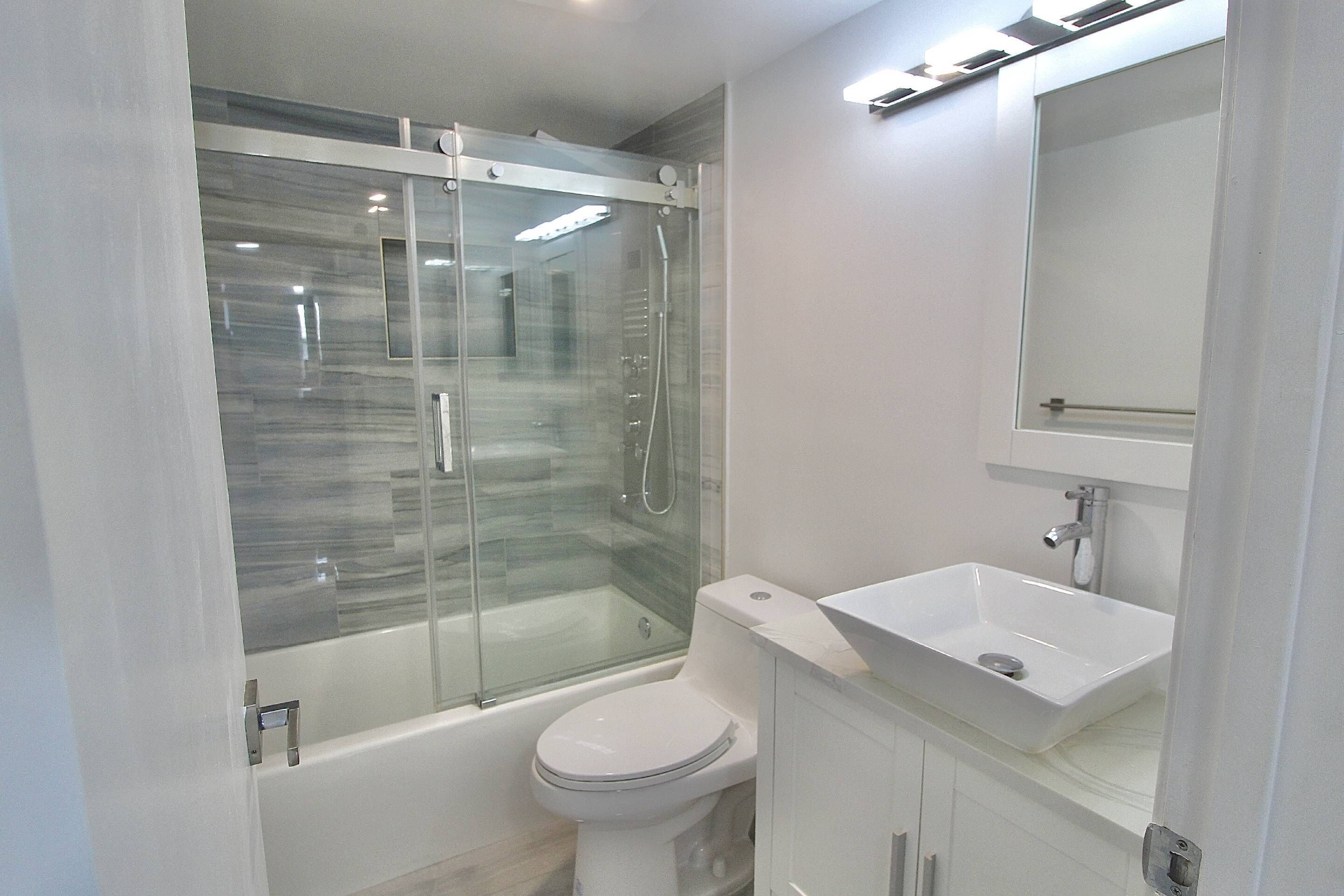A modern bathroom with a glass-enclosed shower, a white toilet, and a sink with a mirror above it.