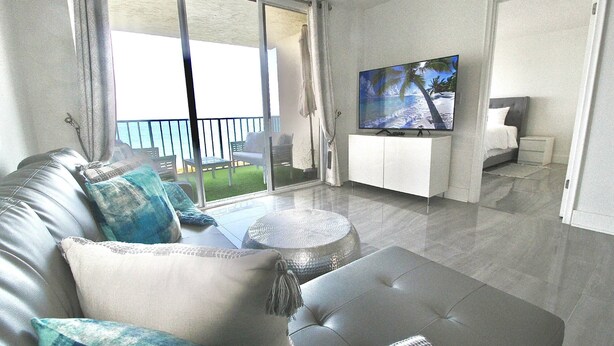 Ein modernes Wohnzimmer mit einer Couch, einem Hocker, einem Flachbildfernseher und einem Balkon mit Blick.
