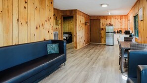 Ein modernes Blockhaus-Interieur mit Holzvertäfelung, einer Couch, einem Esstisch und einer Küchenzeile.