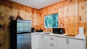 Eine Küche mit Holzwänden, einem Kühlschrank, einer Mikrowelle und einem Fenster mit Blick auf Bäume.